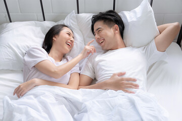 Happy Asian couple lying down smiling and relaxing together in bed.