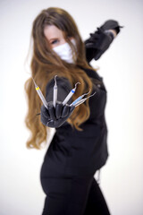 Beautiful woman dentist in black suit with a white mask with flowing hair holds in her hands scaler and curette Hand stretched forward selective focus bright photo of gorgeous woman