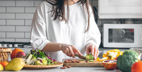 A young woman cutting vegetables for salad in the kitchen.