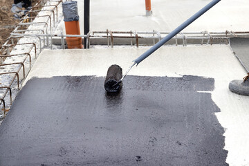 Worker applying a bituminous primer on a Concrete Slab Before Waterproofing - 575970333