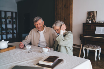 Cheerful mature couple drinking tea at table at home