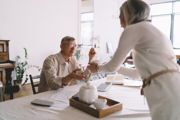 Obraz premium Senior woman offering coffee cup to husband at table
