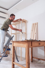 Man assembling new wooden shelf and furniture in the apartment.