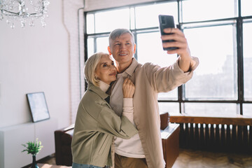 Smiling senior couple taking selfie on cellphone at home