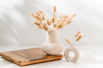 Vase set with dried lagurus grass on wooden podium with copy space on the table with shadows....