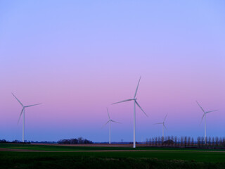 Wind turbines to produce electricity at sunset in a field in France