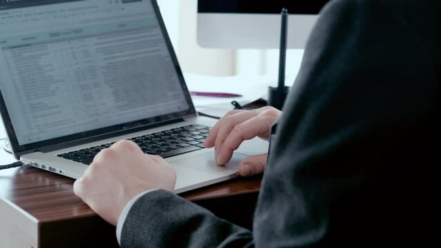 Man in suit typing on a laptop keyboard, working in office. Business analytics in bank sphere, daily report.