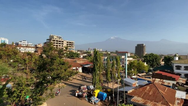 East African town Moshi street traffic with cars, rickshaws and local people daily routine with a huge and  magnificent Kilimanjaro mountain 5895m covered with ice and snows landscape view. Tanzania.