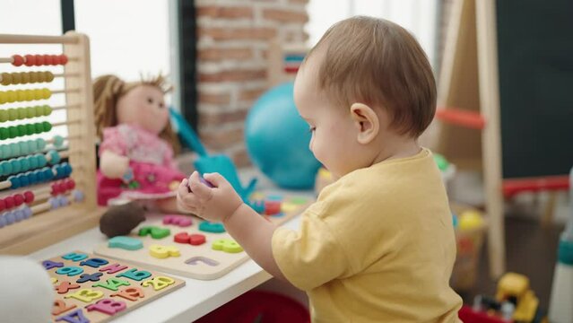 Adorable hispanic baby playing with maths puzzle game standing at kindergarten