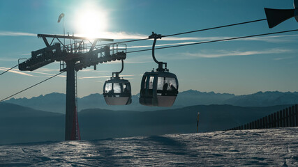 Hanging cable car cabins. Tourists descend to valley during sunset. Winter activities, passion for...