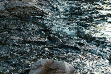 Texture of choppy water on a beach. Waves and sea foam on a rocky beach.