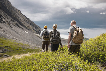 Group of three young tourists walks with small backpacks in mountains