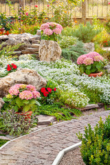 A countryside floral background with blooming flower beds and an ornamental path. An outdoors photo of a backyard in the country. The landscape delivers the summer vibe of gardening at a cottage.