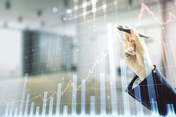 Double exposure of man hand with pen working with virtual creative financial diagram on blurred office background, banking and accounting concept