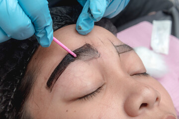 An esthetician applying additional pigment into the already cut skin of the eyebrow of a customer. A typical microblading technique to thicken and complete the brows..