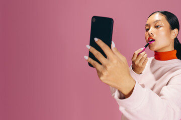 Doing makeup using a smartphone, young woman applies lipstick in a studio