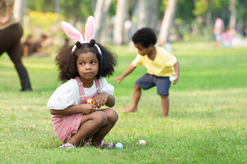 Little African boy and girl wearing bunny ears pick up Easter egg in garden, Easter eggs hunting...