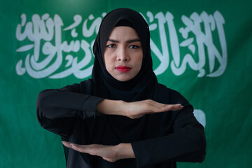 Portrait of Muslim woman wearing black hijab stands in front of the Saudi Arabian flag and hand with the symbol for international women's Day