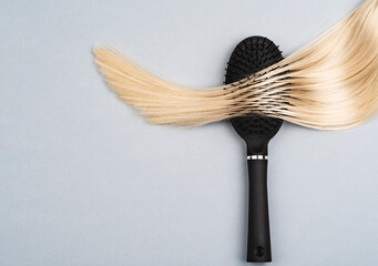Professional haircare equipment. A close-up of shiny, blonde, long, straight hair with healthy structure in a hairbrush, showing the process of salon treatment and hairstyling. Natural, healthy look.