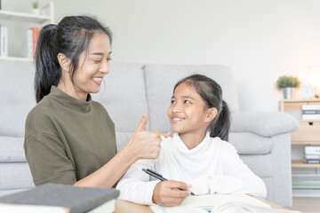 Asian young little girl learn at home. Do homework with kind mother help, encourage for exam. Mom pass on a glass of milk to daughter. Girl happy Homeschool. Mom teach and advice education together.