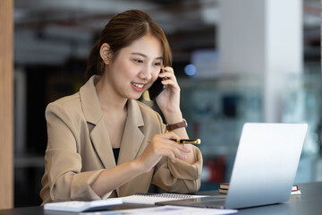 Fototapeta premium Attractive Asian businesswoman in office using smartphone and talking with business partner on mobile phone.