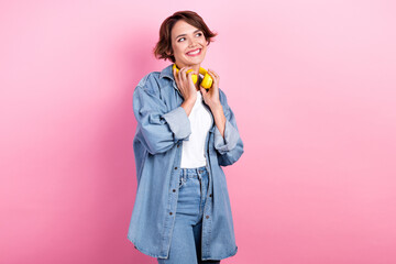 Photo of positive pretty young woman hold new stylish yellow futuristic wireless earphones music lover look mockup isolated on pink color background