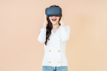 portrait of a young asia woman wearing a white cardigan and VR glasses. She is amazed by what she is seeing. Virtual reality headset. isolated orange background
