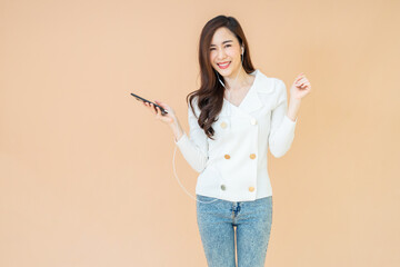 Nice attractive cheerful young girl listening music audio mp3 in earbuds, holding smartphone isolated on orange color background