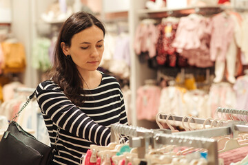 Pregnant woman chooses clothes for her future daughter. Mother doing shopping in baby shop.