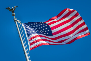 American flag waving on pole with eagle and bright colors against blue sky