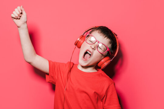 Energetic Boy In Headphones Singing Against Red Background