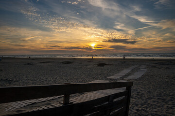 Sunset on the beach with veil clouds. With wooden bridge on the beach.