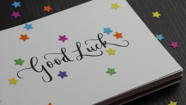 GOOD LUCK lettering in notebook with colorful stars on black wooden desk