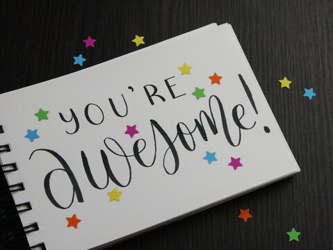 YOU'RE AWESOME! lettering in notebook with colorful stars on black wooden desk