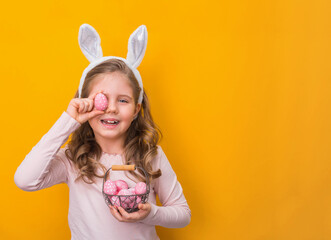 Little girl with bunny ears holding easter eggs on yellow background with copy-space.