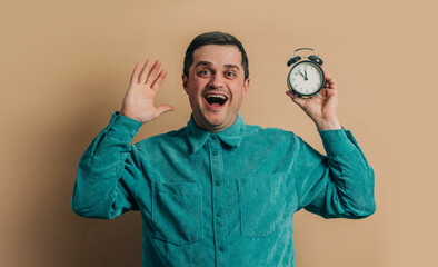 surprised caucasian man in green shirt with vintage alarm clock on brown background