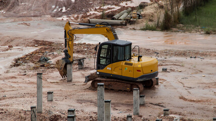 An excavator is working to insert stake or concrete foundation pillars into the ground on a...