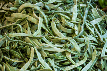 Lots of pods of green beans on market stall for sale.