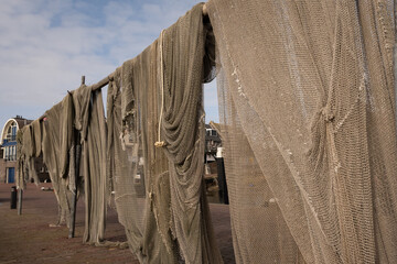 Fishing nets used by commercial Dutch fishermen on trawler boats hang up in Urk Netherlands to dry in sun after washing to maintain the apparatus required for industrial harvesting of the sea water  - obrazy, fototapety, plakaty