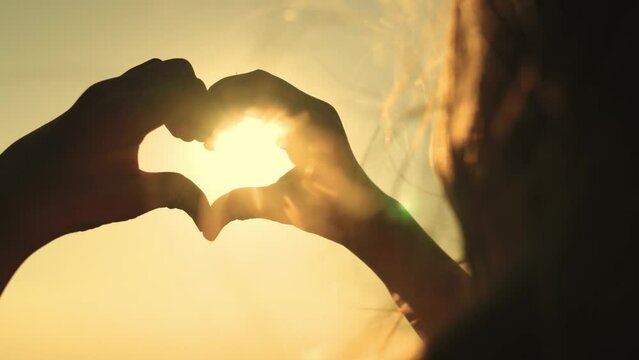 heart sign sunset background. beautiful girl with flowing hair against backdrop sunset sky. love health sign silhouette. Valentine's Day. state mind love. romantic girl glare sun shows heart. concept