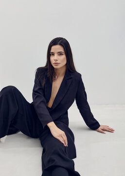 a beautiful woman poses relaxed sitting in a black suit on a light background