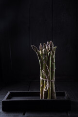 Bundle of fresh asparagus on a wooden table against a dark background.