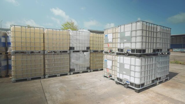 Footage of white IBC Tank for chemical storage and transportation in storage yard with blue sky in background.