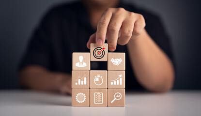 Business goals and marketing strategies. Economic analysis, Company development and success. Wooden cube blocks stack with target and strategy icons. Man selecting target icon on wooden lock. - obrazy, fototapety, plakaty