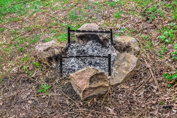 Lightweight portable brazier stands over an extinct campfire inside a stone circle outdoors. Means of cooking in the park or in the forest