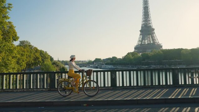 Pretty woman riding a yellow bicycle on a bridge overlooking the Eiffel Tower