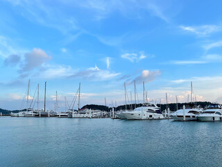 Fototapeta na wymiar View from the sea to the yachts anchored in the harbor. Lowered sails, empty masts are directed to the sky. Sailboats in the marina. Yachting and sailing. Ocean navigation season. Beautiful sunset