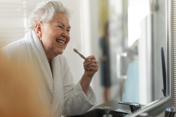 Senior woman cleaning her teeth with wooden brush in bathroom, sustainable lifestyle.