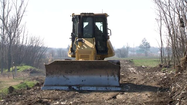 Earth movers leveling ground on road construction in field.
 A bulldozer moves the ground with an attached blade on a worksite. Bulldozer levels and repairs a road

