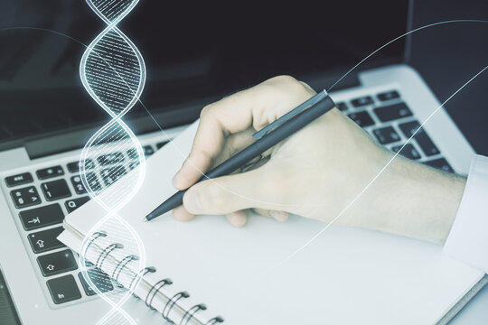 Creative light DNA illustration and hand writing in diary on background with laptop, science and biology concept. Multiexposure